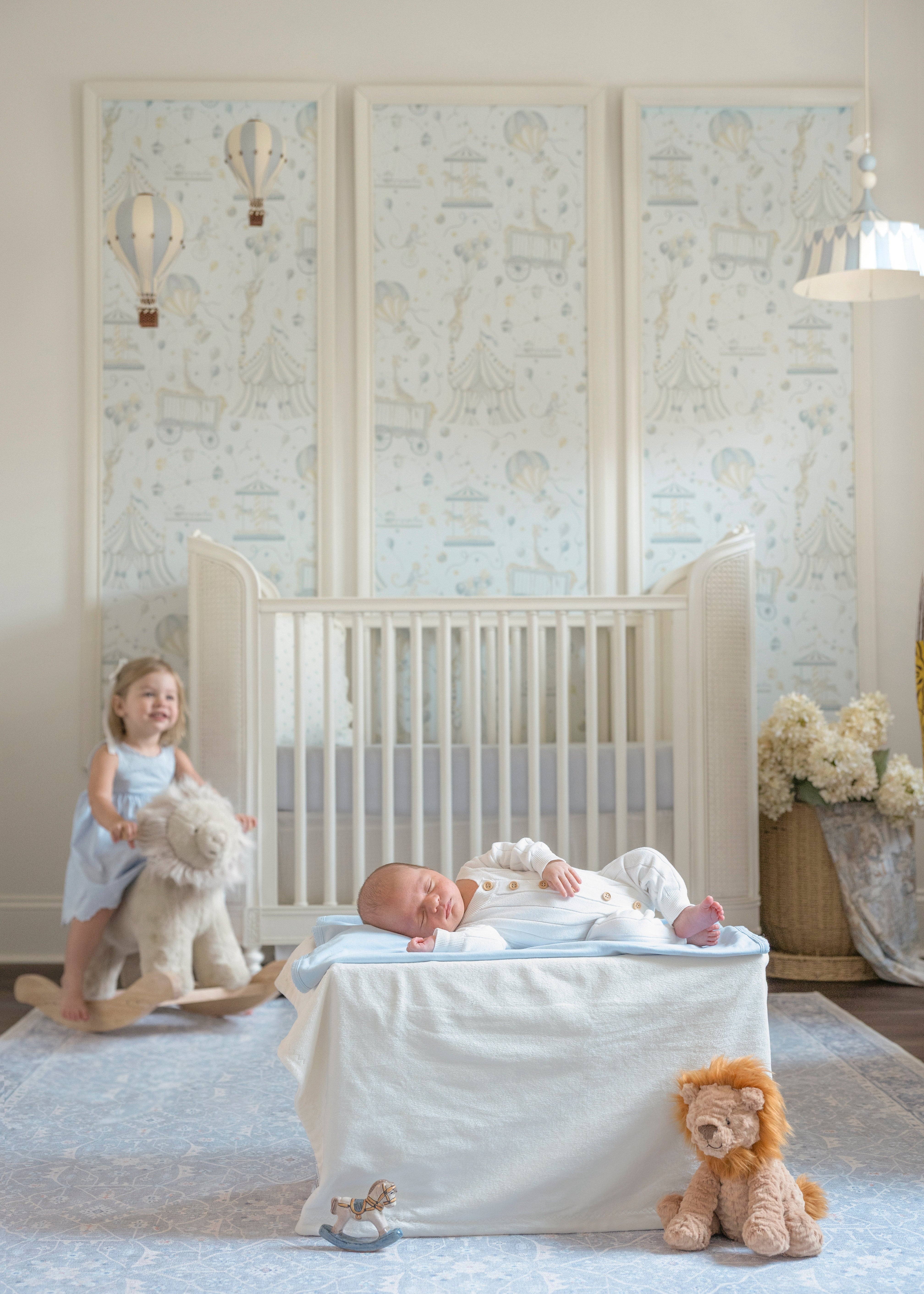 Baby in a crib with toys and a child on a wooden horse in a nursery.
